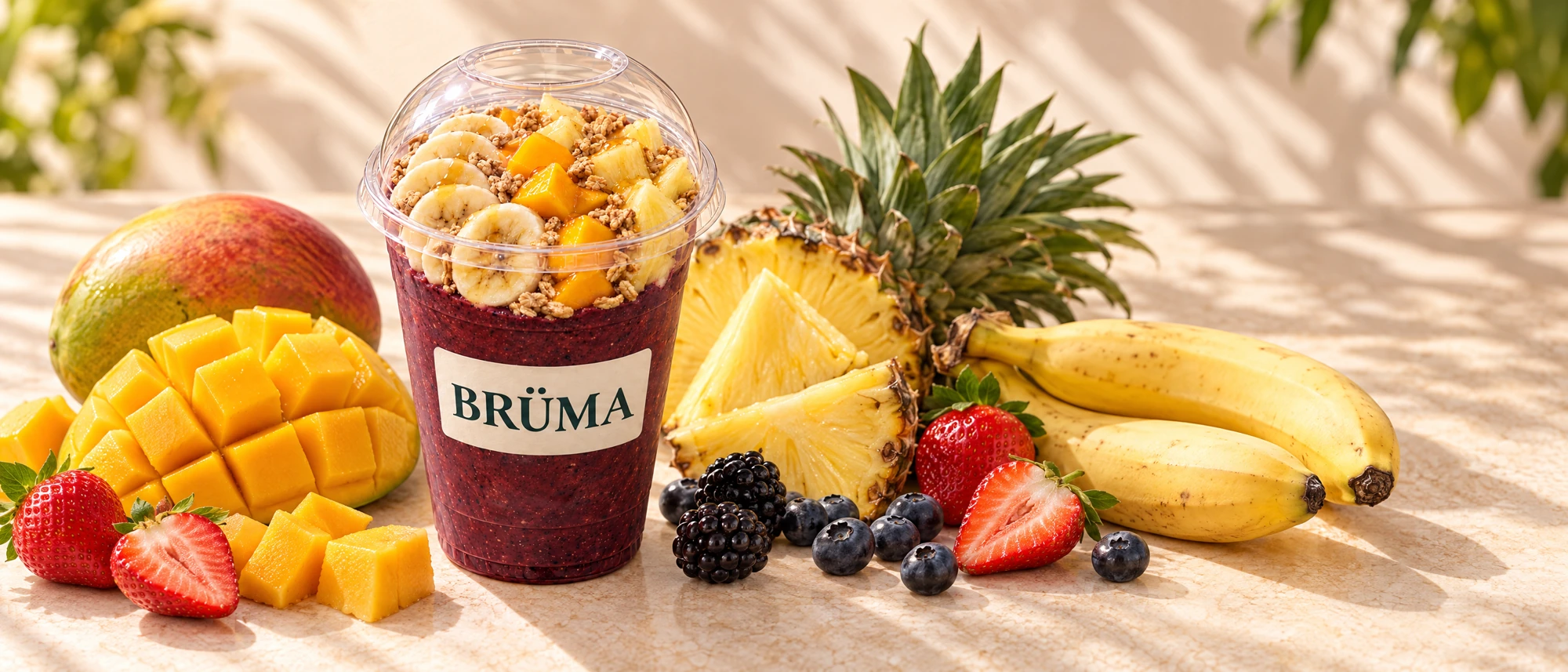 Tropical açaí with granola in a BRÜMA cup, surrounded by mango, pineapple, banana and mixed berries